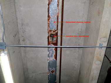 Corroded galvanized channel and abandoned junction box and conduit in gap between T-Joists